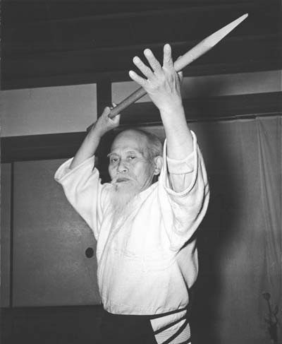 Morihei Ueshiba holding a wooden spear overhead