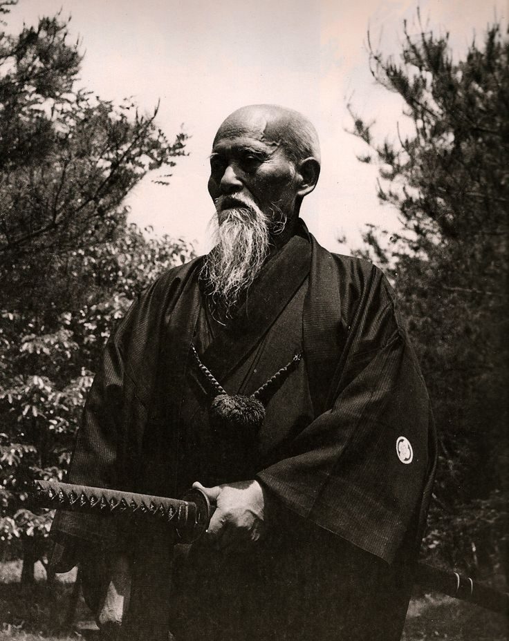 Morihei Ueshiba standing outdoors in a kimono, holding a sword
